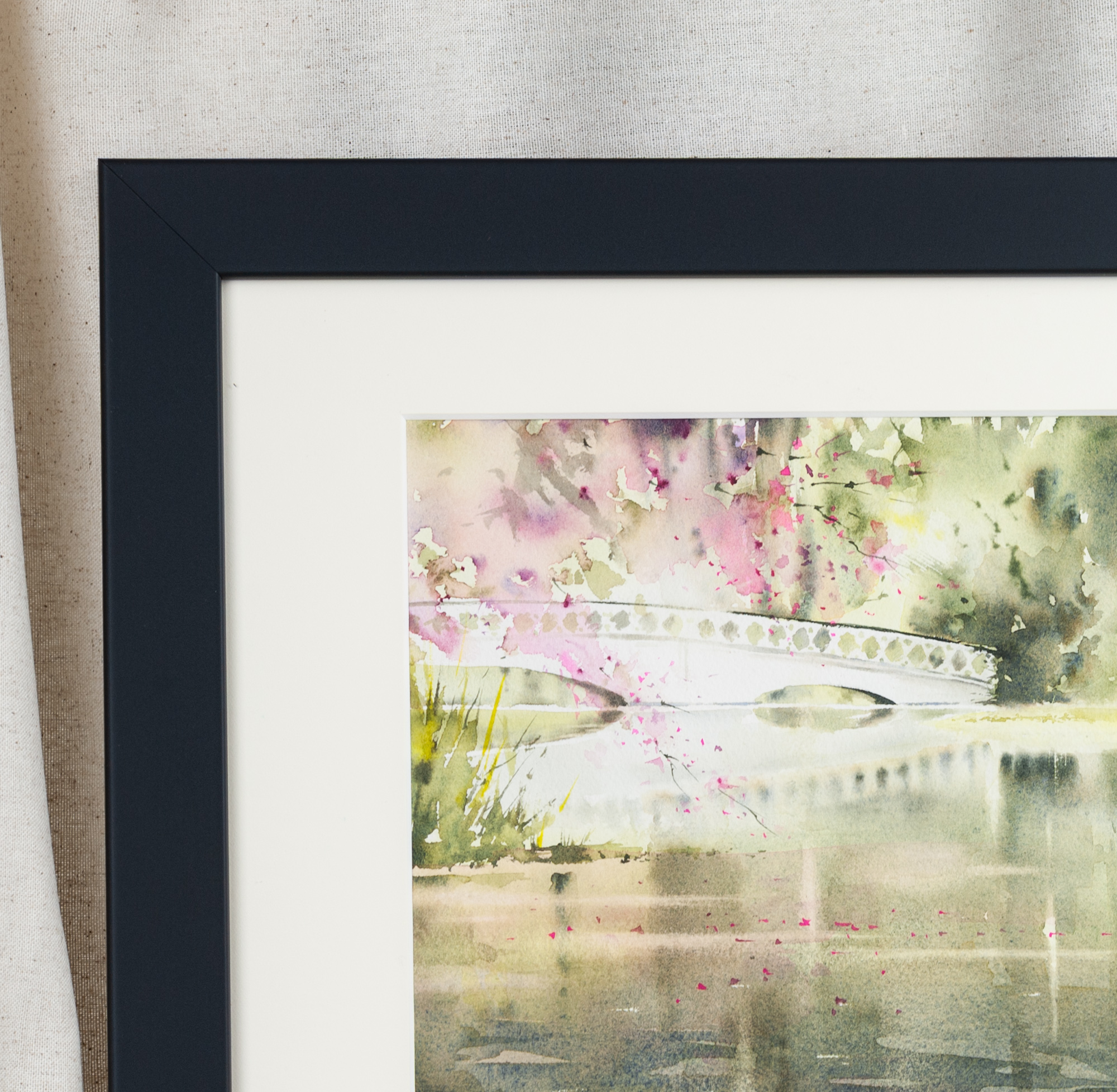 Close-up of framed watercolor painting of the white bridge at Magnolia Plantation in Charleston, with pink blossoms and water reflections highlighting fine detail.