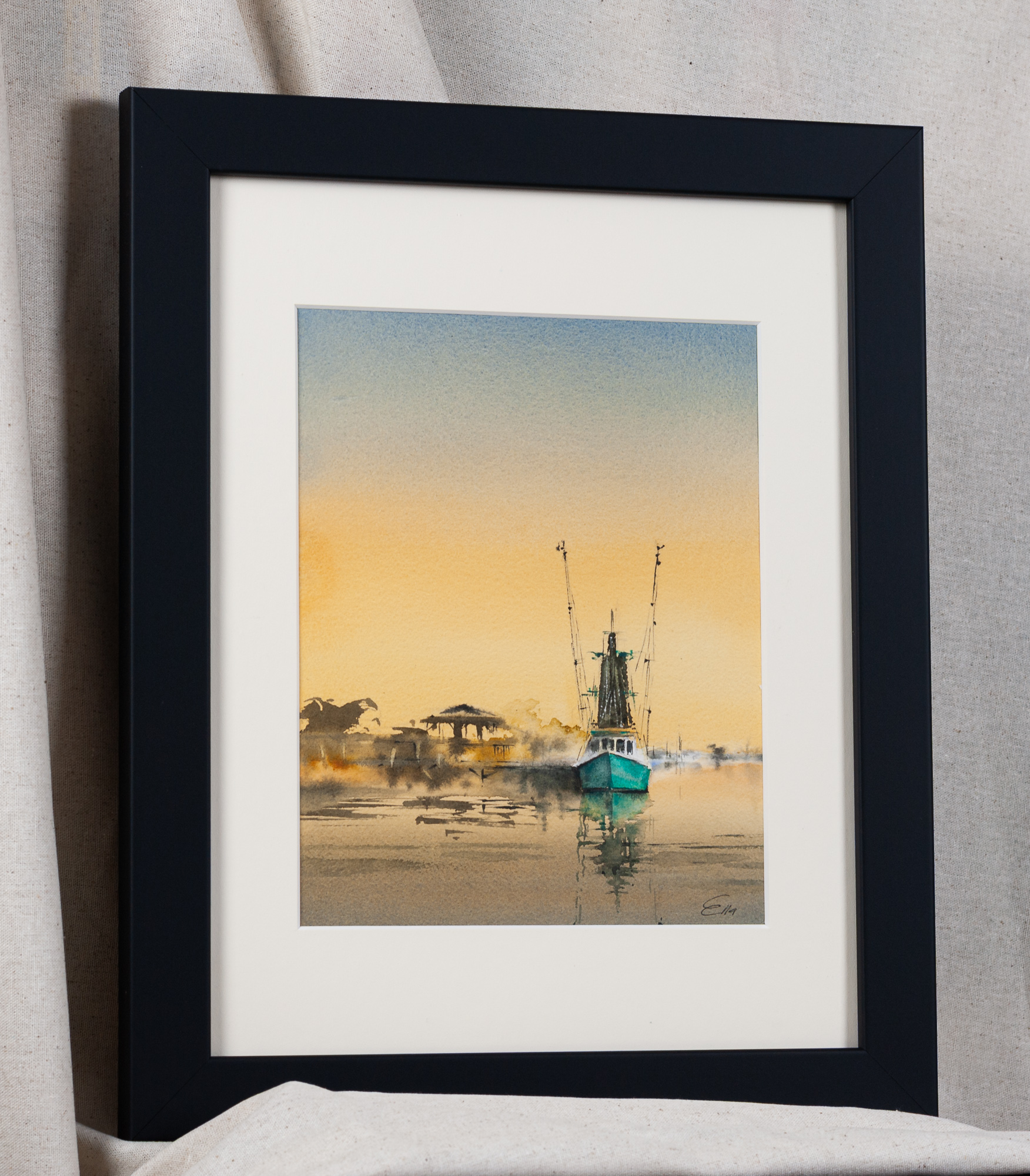 Framed original watercolor painting, Stillness at Shem Creek, featuring a turquoise shrimp boat beneath a golden sunset sky near Charleston, South Carolina, displayed in a black frame with a white mat.